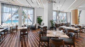En moderne restaurant med havudsigt, striberet trægulv og forskellige siddepladser, inklusiv borde og båse.