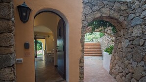 Un arco de entrada da a un espacio exterior cubierto, con paredes de piedra y suelo de baldosas.
