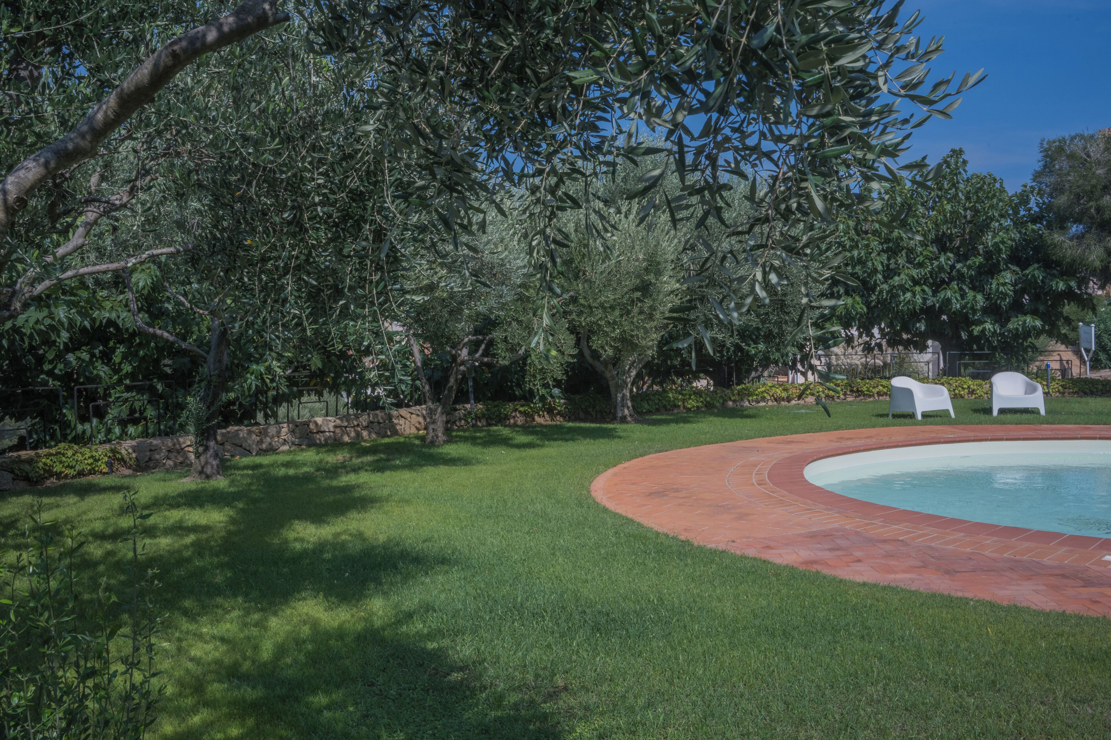 A pool area with a curved brick edge, surrounded by well-maintained grass and trees.