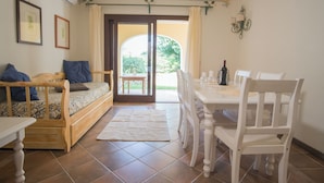 Una habitación acogedora con un sofá de madera, una mesa de comedor con sillas y vistas a un área exterior por una puerta de cristal.
