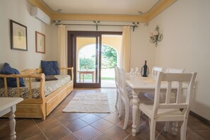 Una stanza accogliente con un divano in legno, un tavolo da pranzo con sedie e vista all'esterno tramite una porta vetrata.