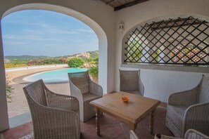 Une terrasse dotée de meubles en osier, d’une table en bois et offrant une vue sur une piscine et un paysage verdoyant.