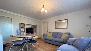 A living room with a sofa, a TV, and a dining area with chairs and a table. - 1 Bed Apartment, Sleeps 2, Free Parking, Tv (Enfield)