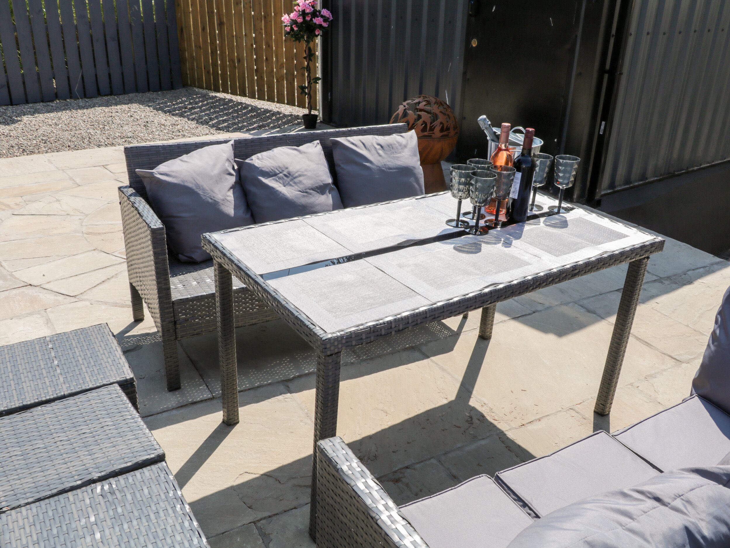 Une terrasse avec une table et des chaises en osier, une plante en pot et un barbecue.