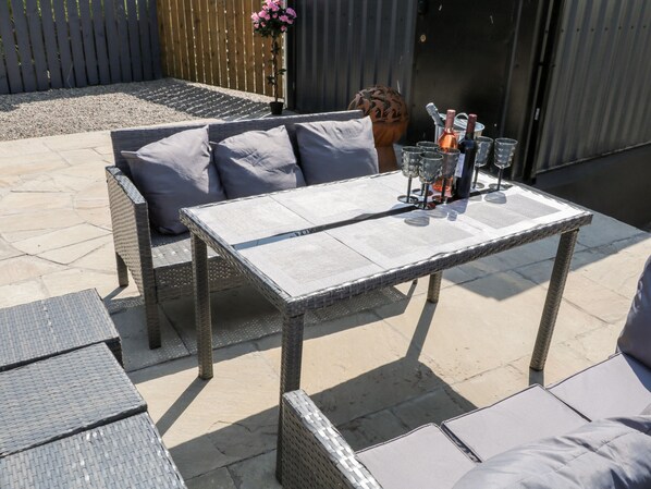 A patio with a wicker table and chairs, a potted plant, and a grill.