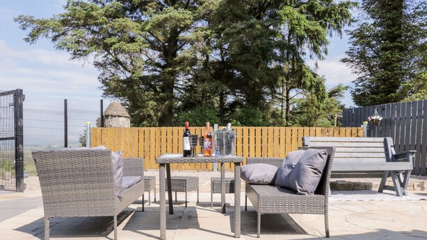An outdoor patio with wicker furniture, a table, and two bottles of wine. - Peter's Farmhouse (Cookstown)