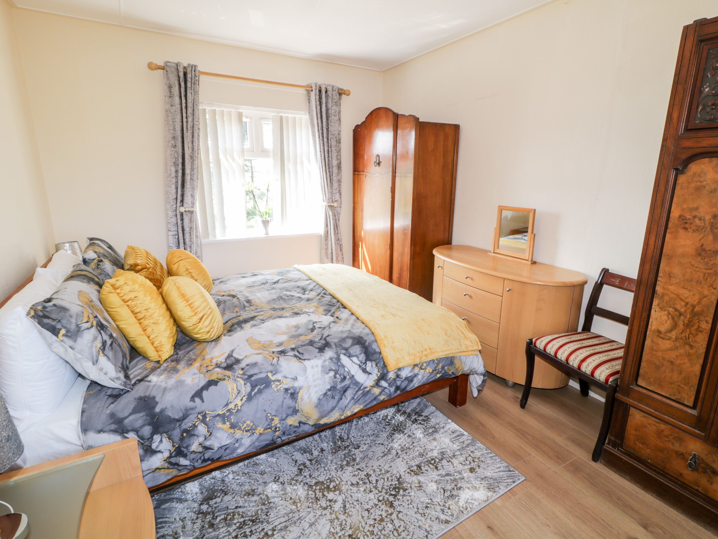 A bedroom with a bed, a wooden dresser, a chair, and a window with curtains.