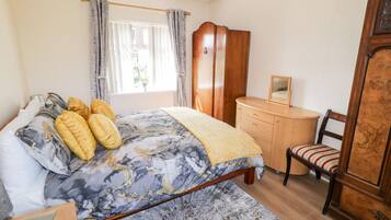 A bedroom with a bed, a wooden dresser, a chair, and a window with curtains.