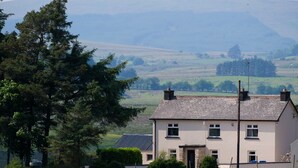 A two-story house with a stone foundation and a tiled roof, surrounded by a grassy field and trees. - Peter's Farmhouse (Cookstown)