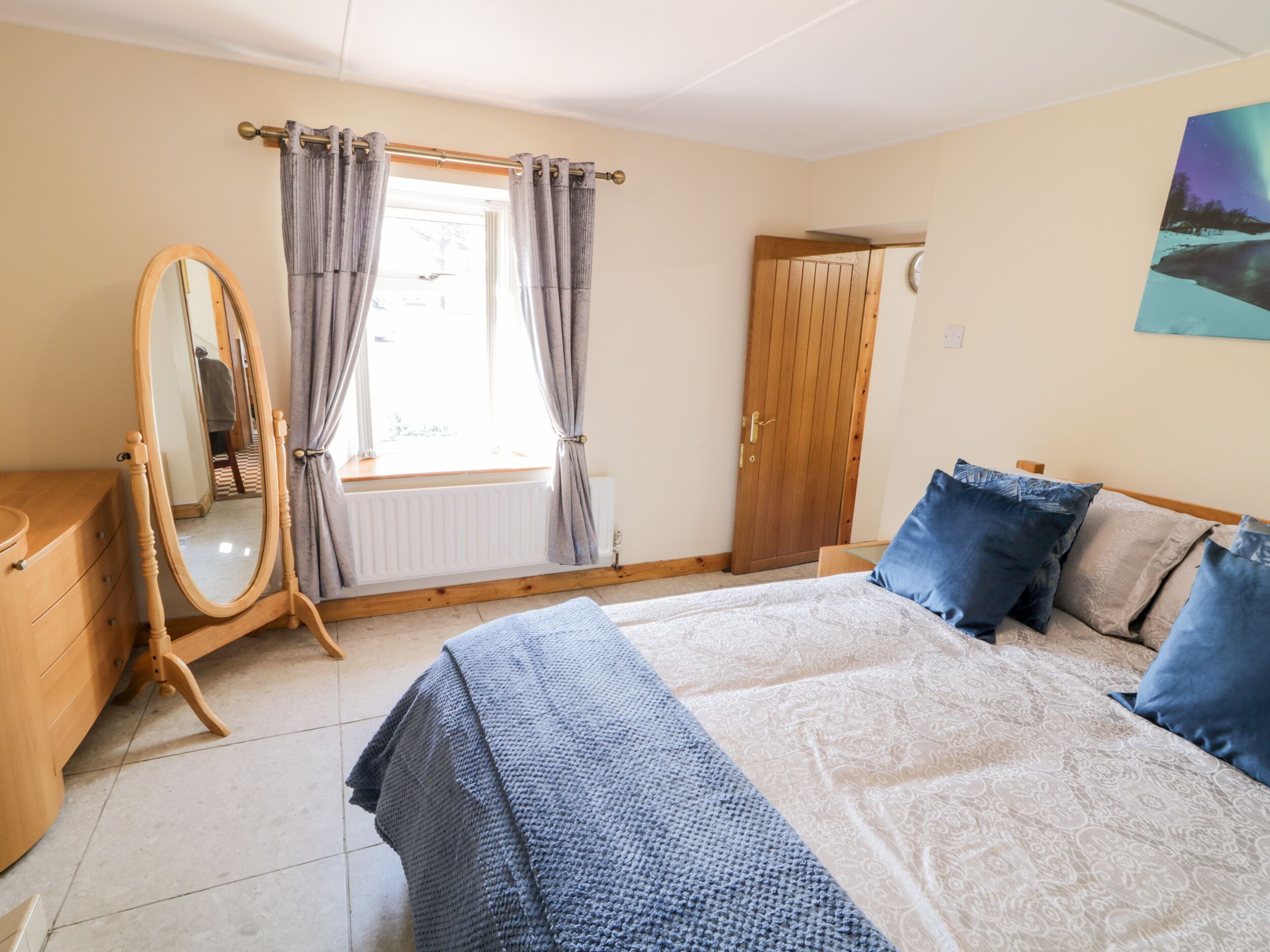 Ein Schlafzimmer mit Bett, Kommode, Spiegel und einem Fenster mit Vorhängen.
