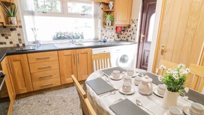 A kitchen with wooden cabinets, a sink, and a dining area set for tea service. - Peter's Farmhouse (Cookstown)