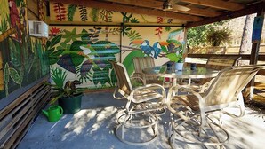 A covered patio with a mural, wicker chairs, a glass table, and a green watering can.