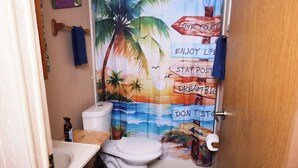A bathroom with a toilet, sink, and shower curtain depicting a beach scene with motivational phrases.