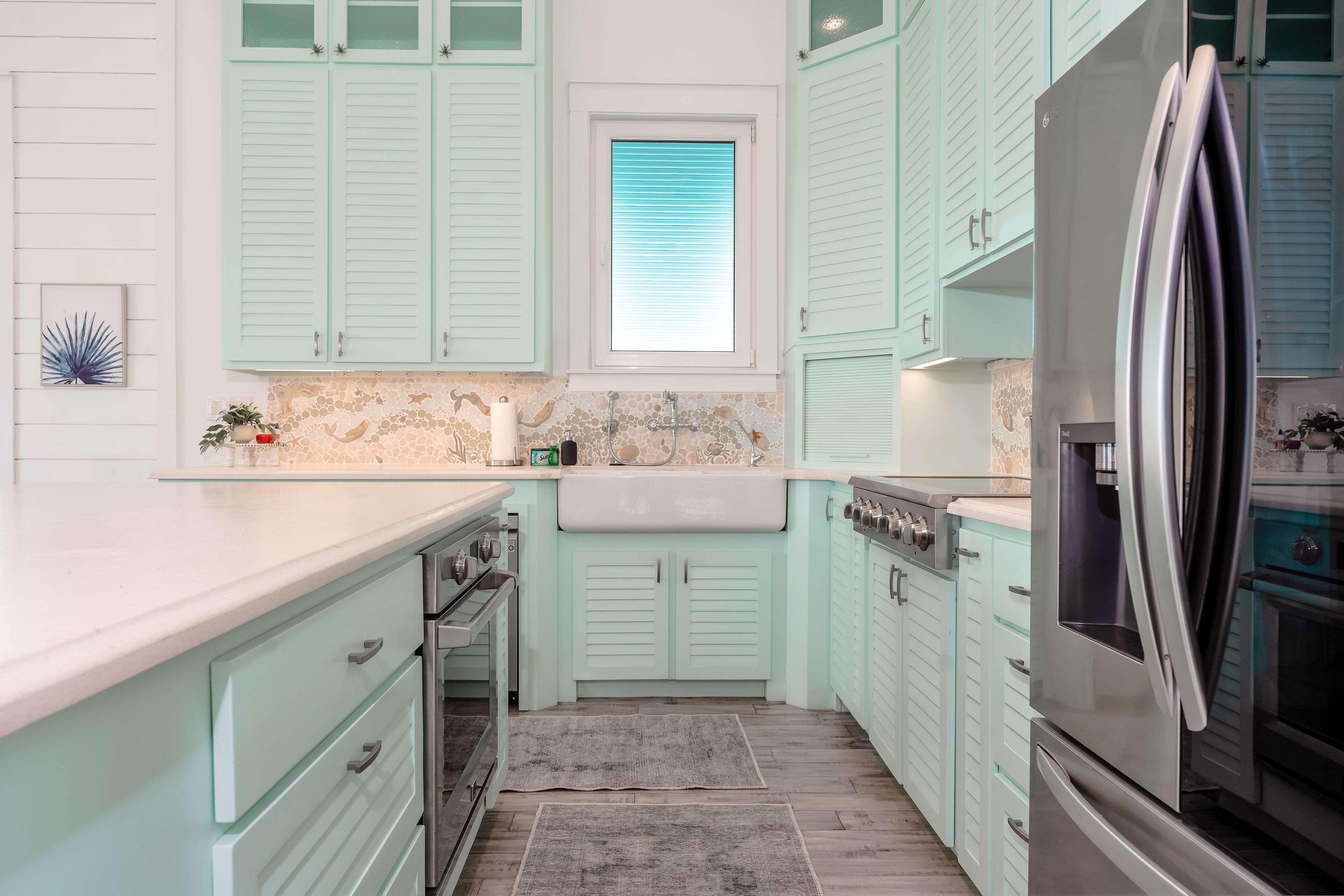 A kitchen with light green cabinets, a stainless steel refrigerator, and a stone backsplash.