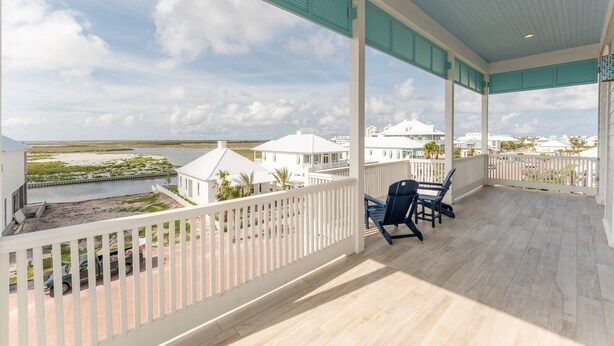 A covered balcony with a view of a beach and white buildings.