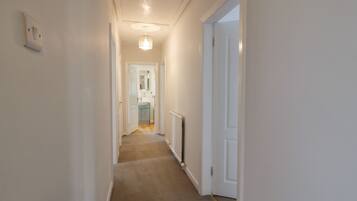 A narrow hallway with carpeted flooring, white walls, and a door leading to a bathroom with a sink and mirror.