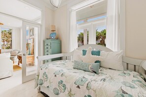 Une chambre à coucher avec un lit, une commode et une fenêtre donnant sur des palmiers.