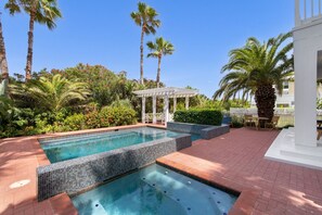 Una piscina con bordes de azulejos, rodeada de palmeras y un pérgola.