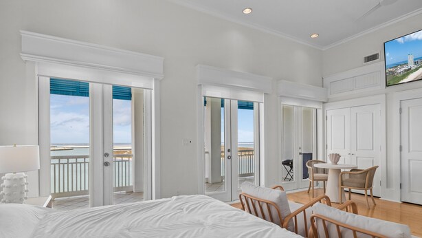 A spacious bedroom with a large bed, a balcony with a view of the sea, and a dining area with wicker chairs. - Avalon - Townhouse At The Shores 4 Bedroom Home by RedAwning (South Padre Island)