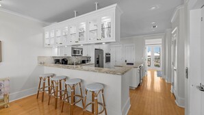 A spacious kitchen with white cabinetry, a central island with stools, and a wooden floor. - Avalon - Townhouse At The Shores 4 Bedroom Home by RedAwning (South Padre Island)