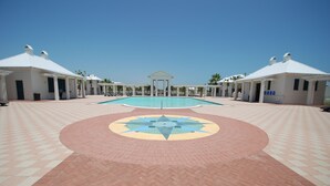 A pool area with a geometric tile design, two white buildings with columns, and a clear blue sky. - Avalon - Townhouse At The Shores 4 Bedroom Home by RedAwning (South Padre Island)