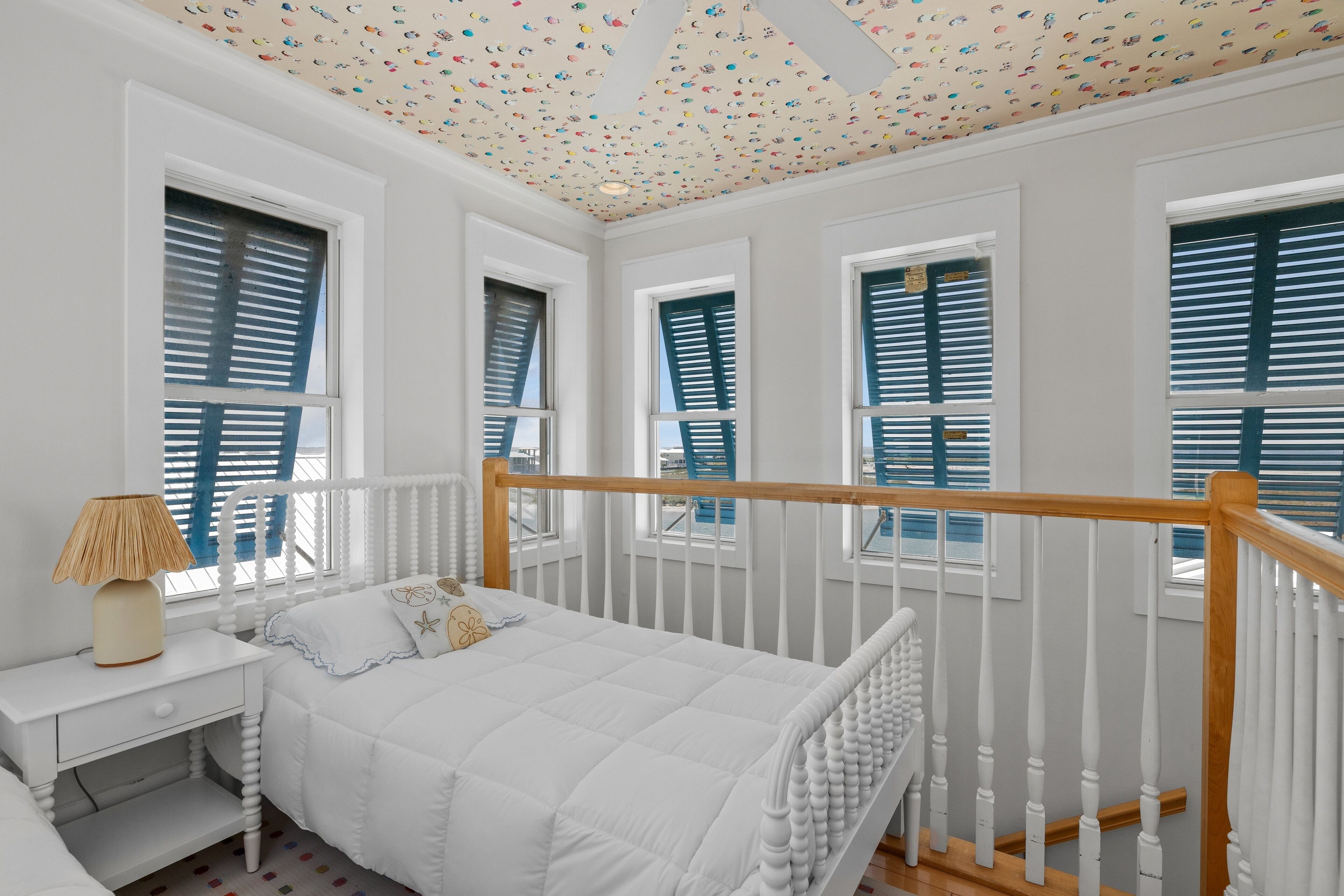Un dormitorio blanco con un cabecero de madera, una mesita de noche y un ventilador de techo.
