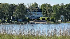 A large white building with a symmetrical facade, surrounded by lush greenery and a calm body of water.