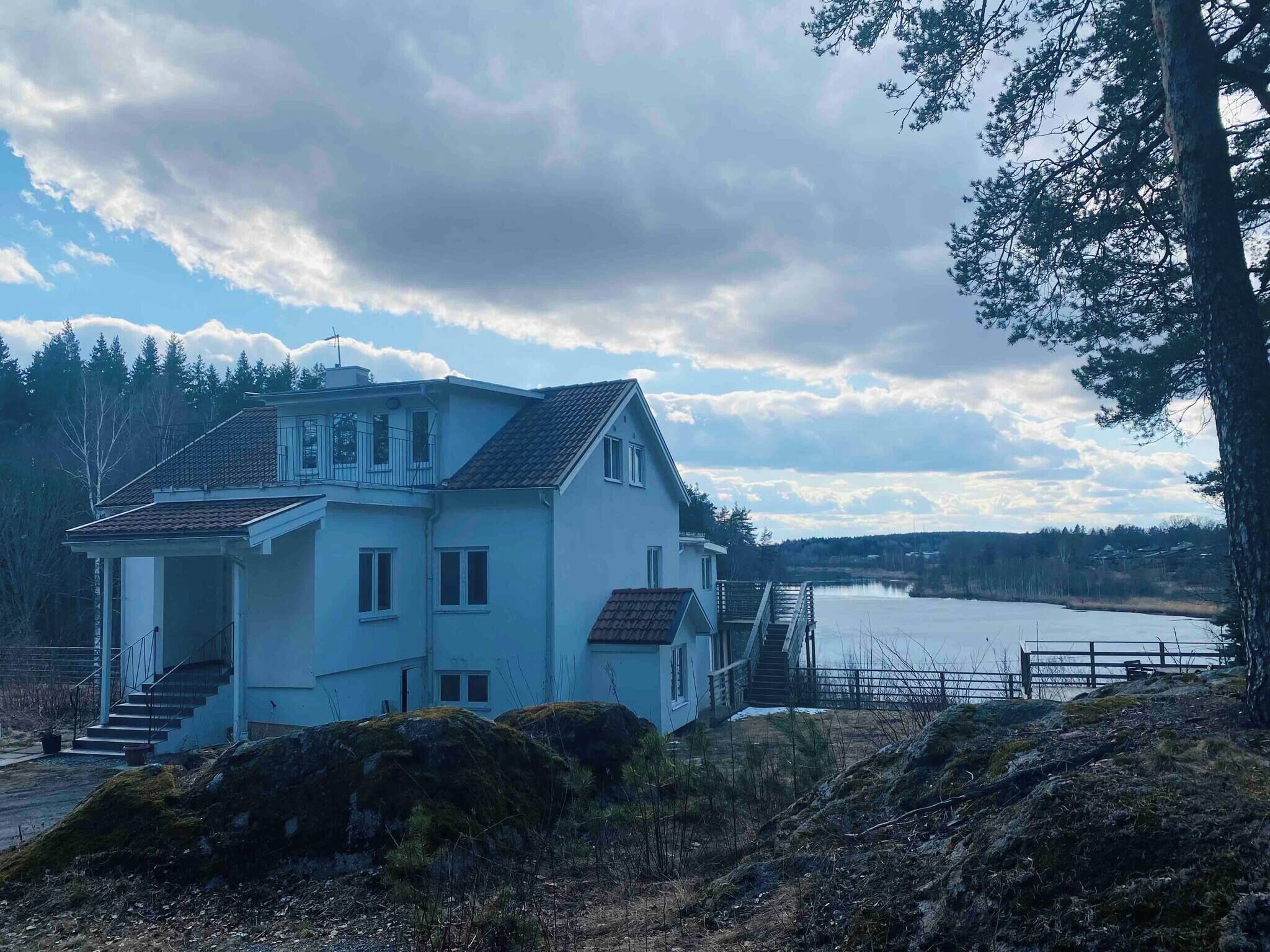 A two-story house with a balcony, situated near a lake with a wooden dock.