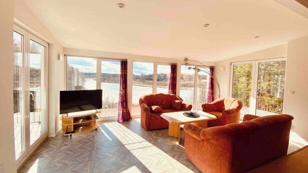 A spacious living room with large windows, a flat-screen TV, and a sofa set.