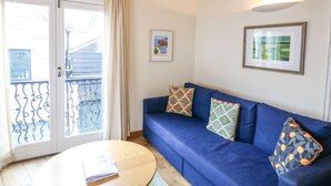 A room with a blue sofa, a round wooden table, and a balcony with metal railings. - The Loft Cottage (Totnes)