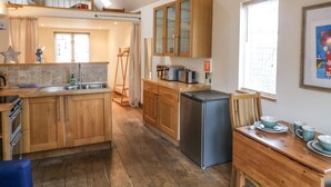 A spacious kitchen with wooden cabinets, a stainless steel refrigerator, and a dining area with a table set for four. - The Loft Cottage (Totnes)