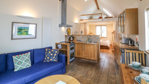 A compact kitchen with wooden cabinets, a built-in oven, and a central island with a sink. - The Loft Cottage (Totnes)