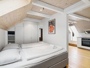 A bedroom with a loft-style ceiling, a bed, a wardrobe, and a kitchen area. - Charming Rooftop Apartment In Heart Of Stavanger (Stavanger)