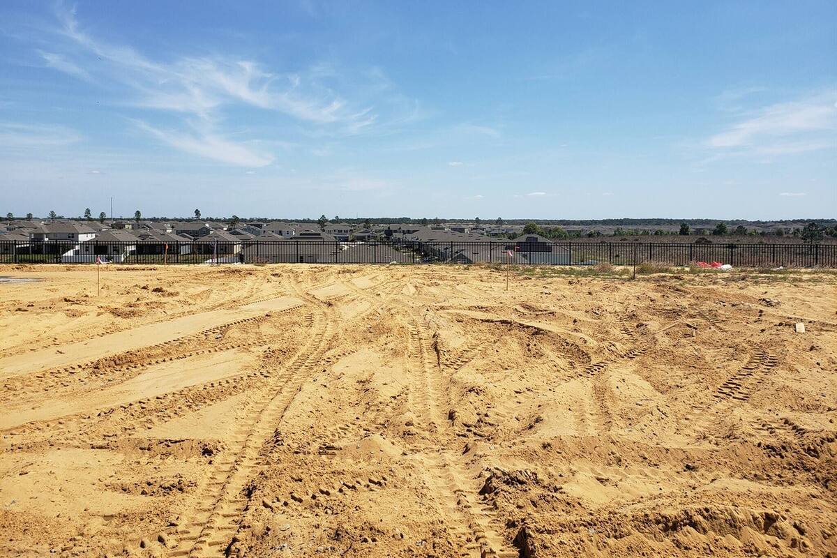 A construction site with a fenced area, tire tracks, and a distant view of residential buildings.