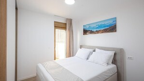 A bedroom with a bed, a window with curtains, a painting on the wall, and a ceiling light. - Salt&soul Residence Three-bedroom Apartmant (Povljana)