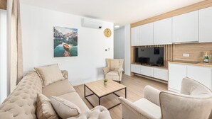 A modern living room with a sofa, chairs, a coffee table, and a painting on the wall. - Salt&soul Residence Three-bedroom Apartmant (Povljana)