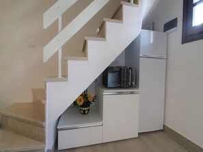 Kitchen area with microwave and refrigerator, adjacent to a staircase with white railings.