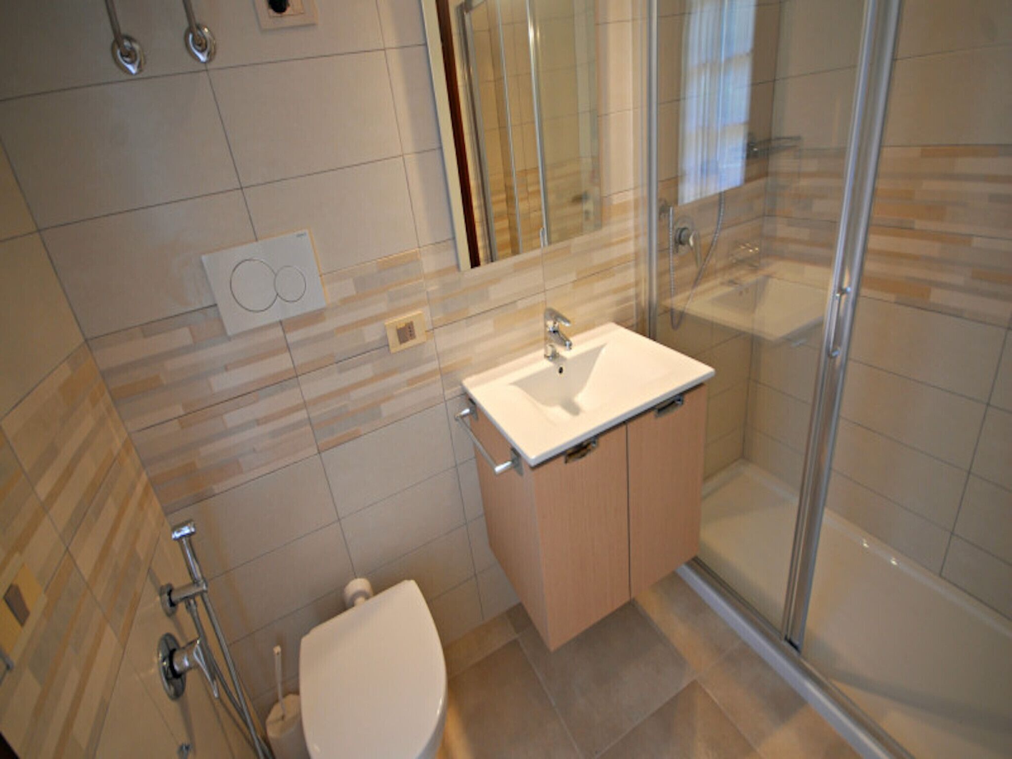 Een moderne badkamer met een glazen douchecabine, een witte wastafel en een toilet.