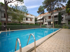 A swimming pool with metal ladders, surrounded by a brick walkway and trees. - Relaxing Villa With Shared Pool (Lignano Sabbiadoro)