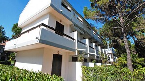 A modern multi-story building with balconies, surrounded by greenery and trees. - Relaxing Villa With Shared Pool (Lignano Sabbiadoro)