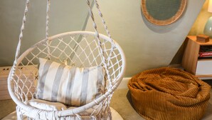 A white macrame hanging chair with a striped cushion, a brown woven pouf, and a round woven wall hanging. - Corner House (Saltburn-by-the-Sea)