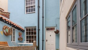 A narrow alleyway with a blue building, a white door labeled "Corner House," and a wooden bench. - Corner House (Saltburn-by-the-Sea)