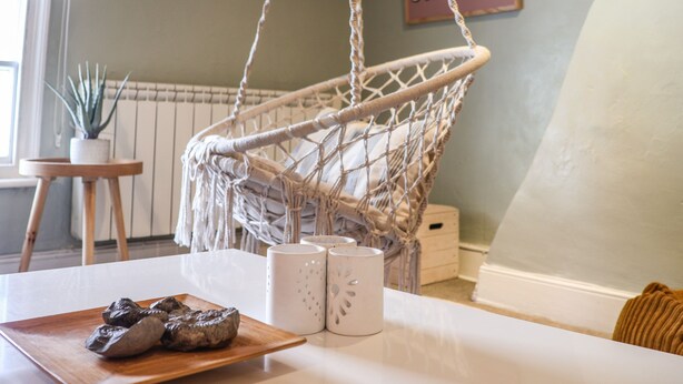 A room with a macrame hanging chair, a small table with a wooden tray and salt and pepper shakers, and a potted plant. - Corner House (Saltburn-by-the-Sea)