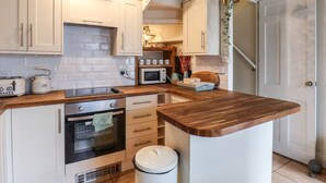 A kitchen with white cabinets, a wooden countertop, a built-in oven, a microwave, and a kettle. - Corner House (Saltburn-by-the-Sea)