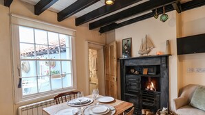 A dining area with a table set for four, a fireplace, and a window with a view of a building with a tiled roof. - Corner House (Saltburn-by-the-Sea)