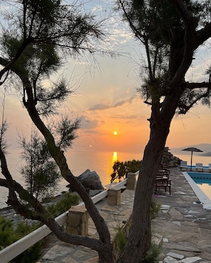 Vista del atardecer con una piscina de piedra y sillones de descanso.