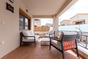 Ein Balkon mit Sitzmöbeln, ein Fenster mit Jalousien und Blick auf umliegende Gebäude.