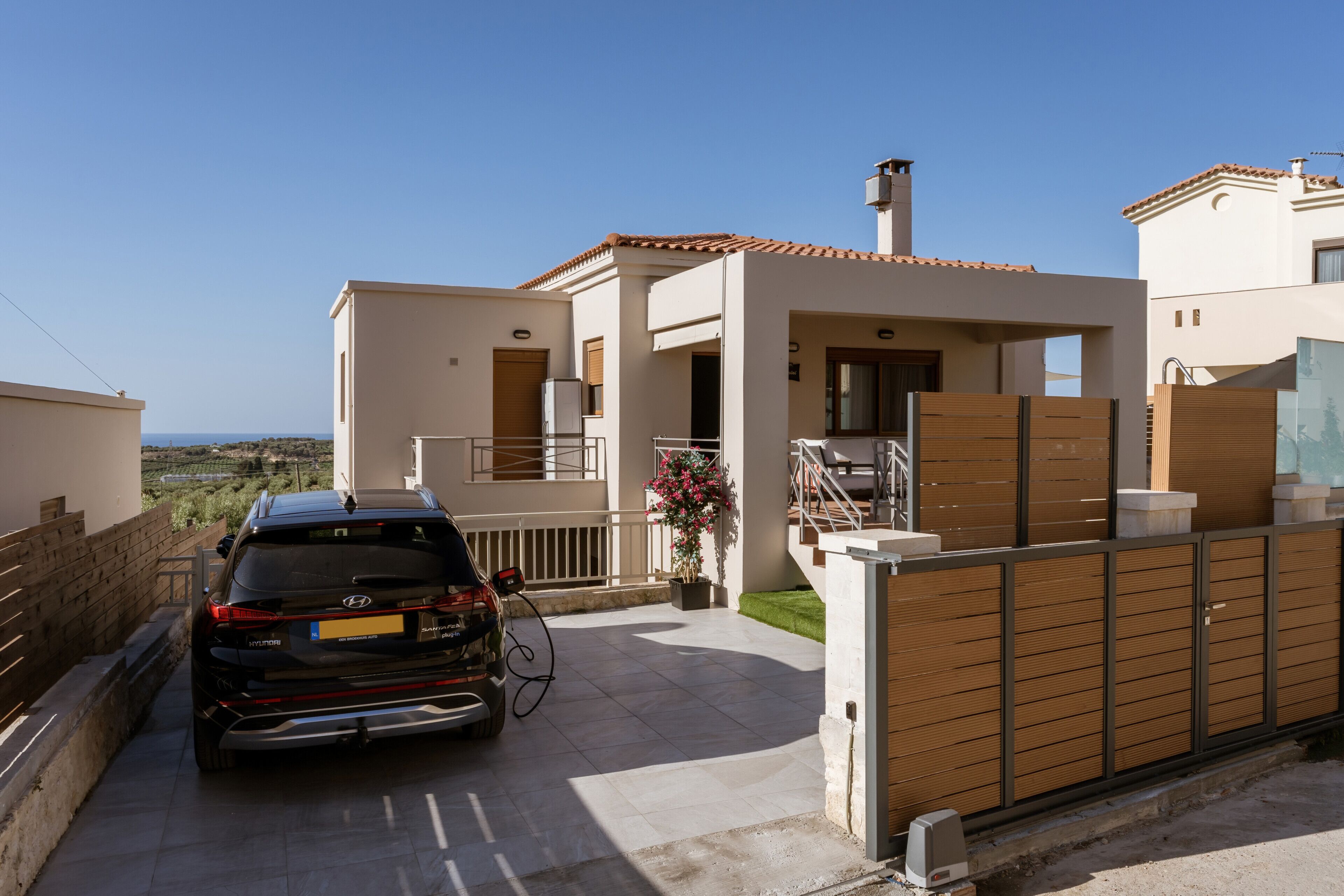 A modern villa with a car parked in the driveway, a staircase leading to the entrance, and a view of the surrounding landscape.