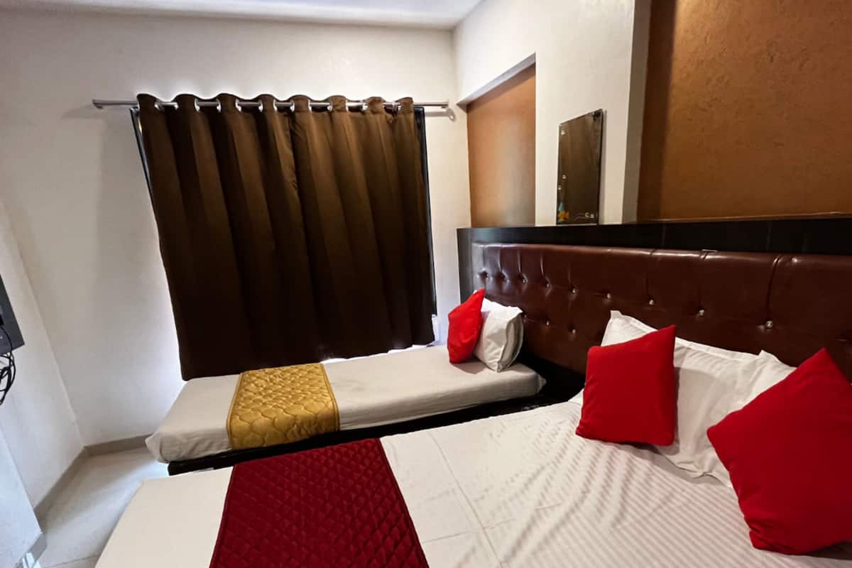 A hotel room with a bed, a headboard, a window with curtains, and a wall-mounted mirror.