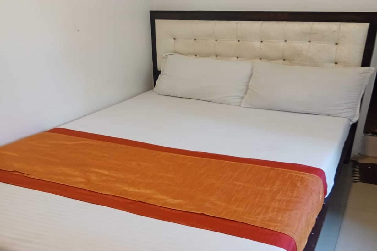 A bed with a white mattress and orange bedspread, a tufted headboard, and a plain white wall.